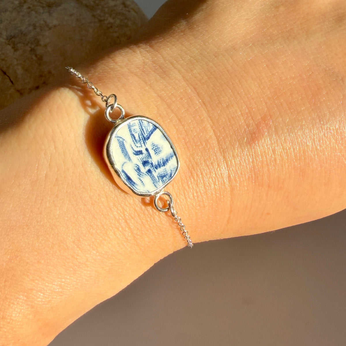 A sterling silver chain bracelet with a blue and white patterned pendant, shown worn on a person's wrist.